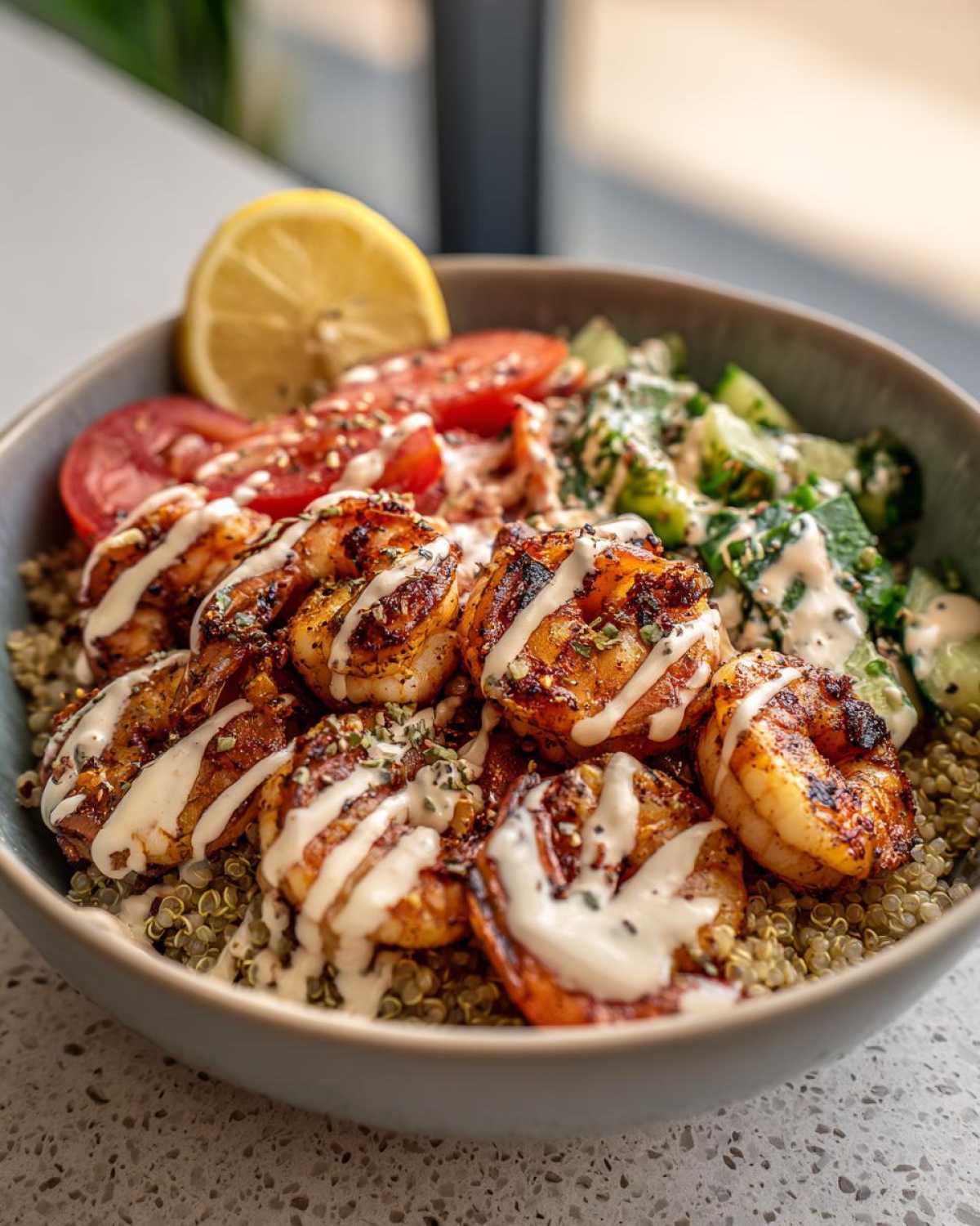 Close-up of a delicious grilled shrimp bowl featuring seasoned grilled shrimp over quinoa, topped with creamy sauce, tomatoes, and cucumber.