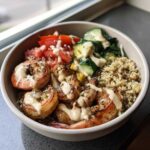 Close-up of a vibrant grilled shrimp bowl featuring seasoned shrimp, quinoa, tomatoes, cucumbers, and a creamy dressing.