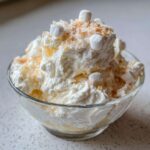 A serving of creamy Hawaiian pineapple coconut fluff topped with whipped cream, toasted coconut, and mini marshmallows.