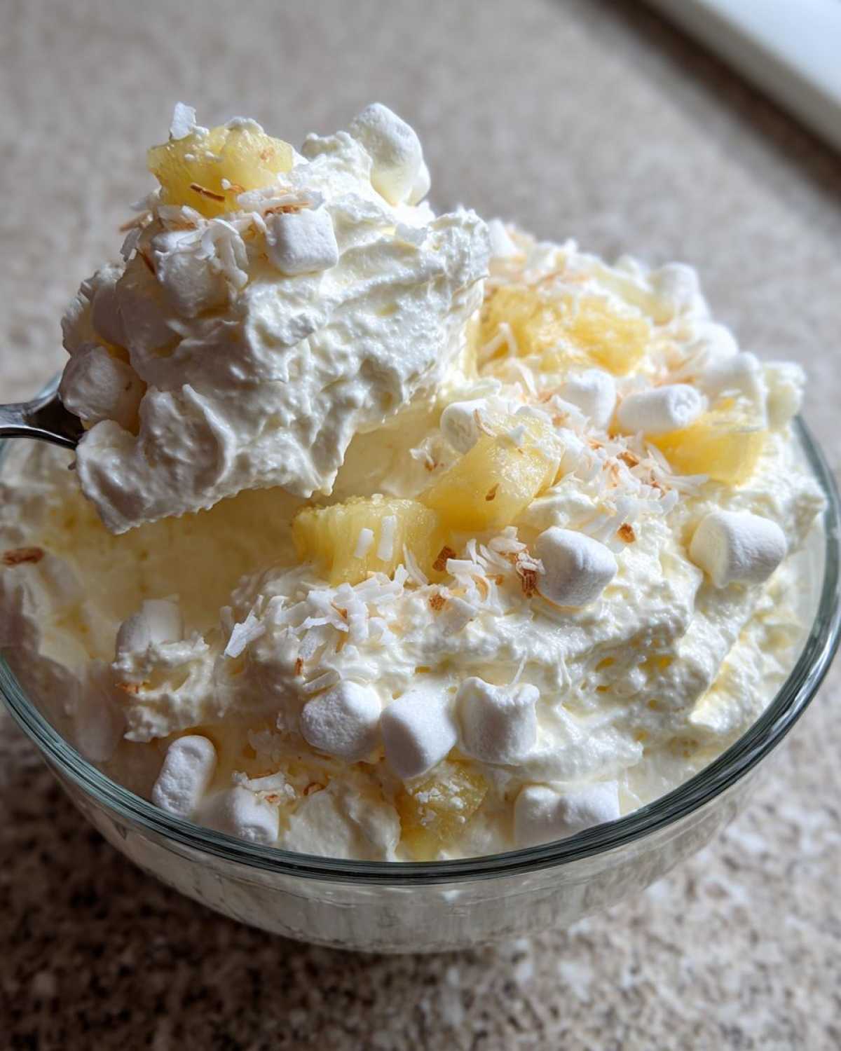 A spoonful of creamy Hawaiian pineapple coconut fluff topped with marshmallows and coconut flakes.