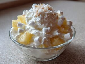 A close-up of a serving of hawaiian pineapple coconut fluff topped with whipped cream, mini marshmallows, and toasted coconut.