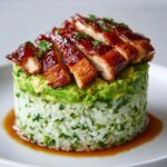 Close-up of a perfectly stacked honey lime chicken & avocado rice stack, featuring glazed chicken slices over avocado and cilantro rice.
