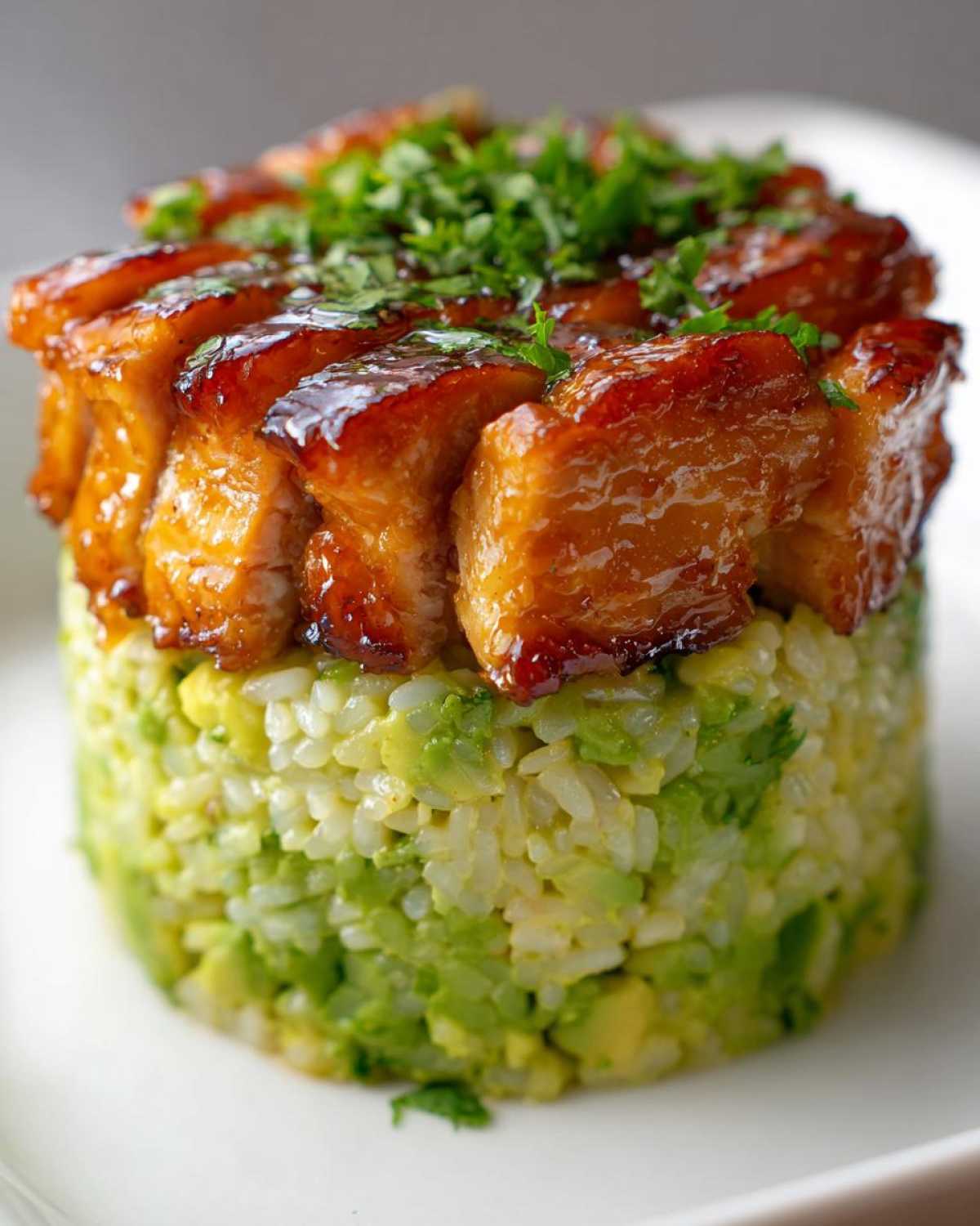 Close-up of a perfectly stacked honey lime chicken & avocado rice stack, topped with fresh herbs.