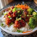 Close-up of sticky, glazed honey sriracha chicken served over white rice with broccoli and carrots.