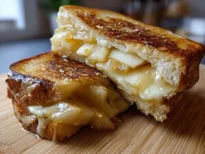 Close-up of a grilled hot honey apple cheddar sandwich, cut in half, showing melted cheese and spiced apple slices.
