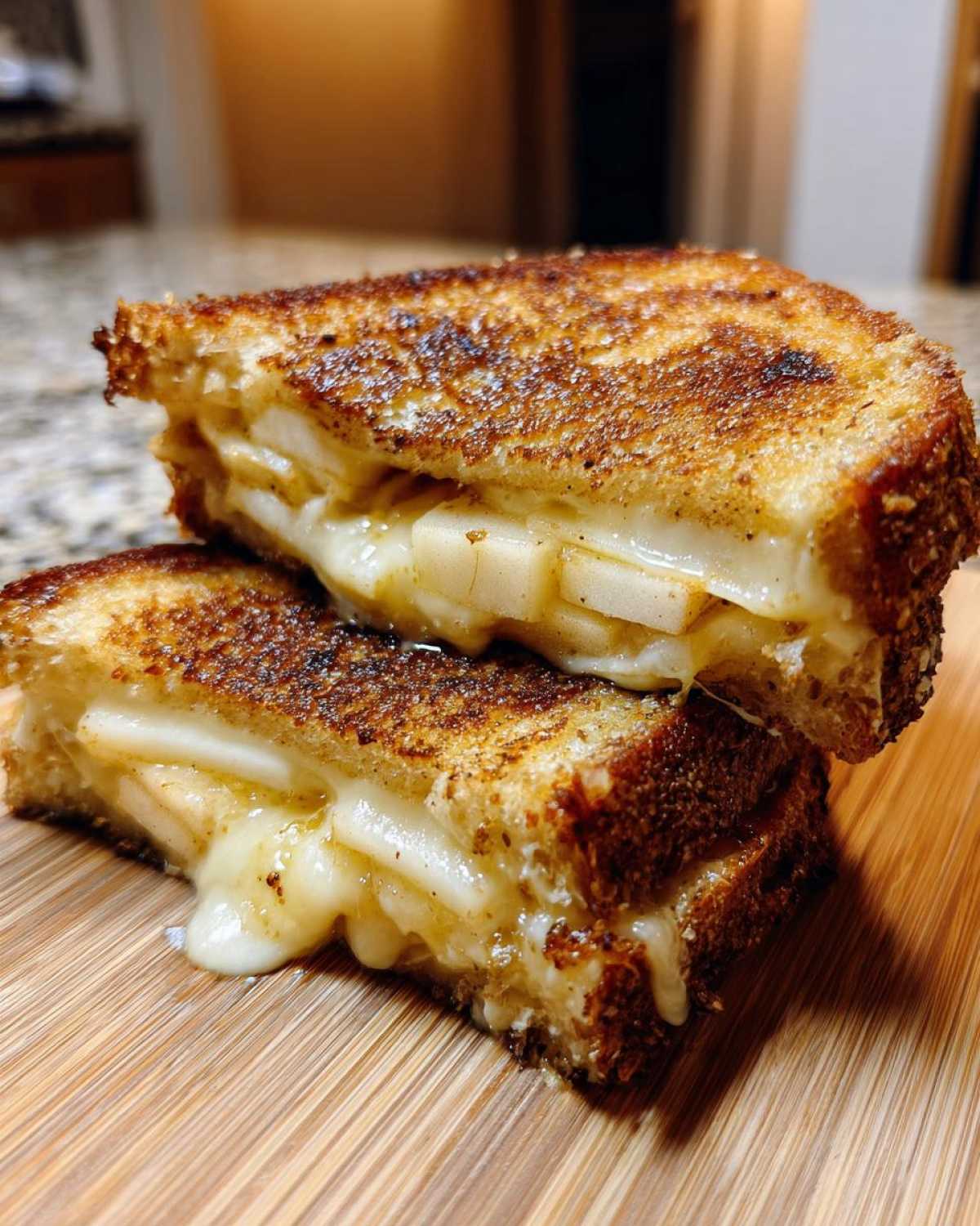 Close-up of a hot honey apple cheddar sandwich cut in half, showing melted cheese and apple slices.
