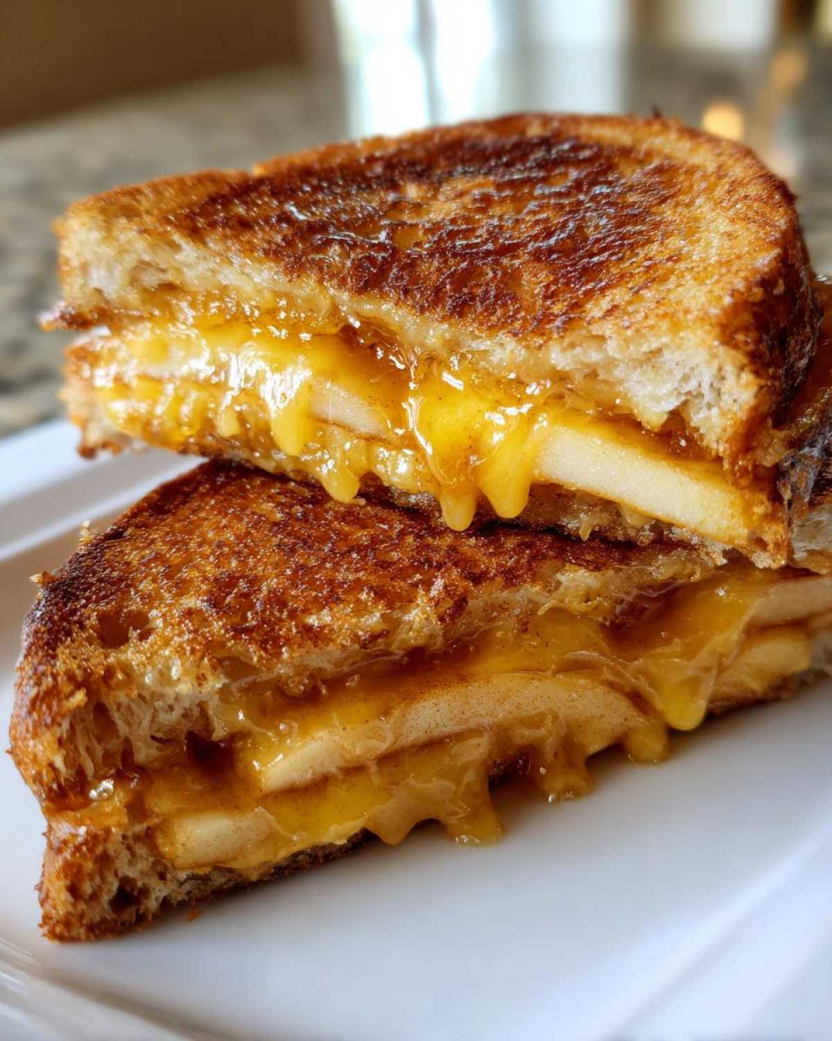 Close-up of a grilled hot honey apple cheddar sandwich cut in half, showing melted cheese and apple slices oozing out.