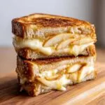 Two halves of a grilled hot honey apple cheddar sandwich stacked, showing melted cheese and apple slices drizzled with honey.