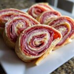 Close-up of several sliced Italian pinwheels showing layers of salami, ham, and cheese rolled in dough.