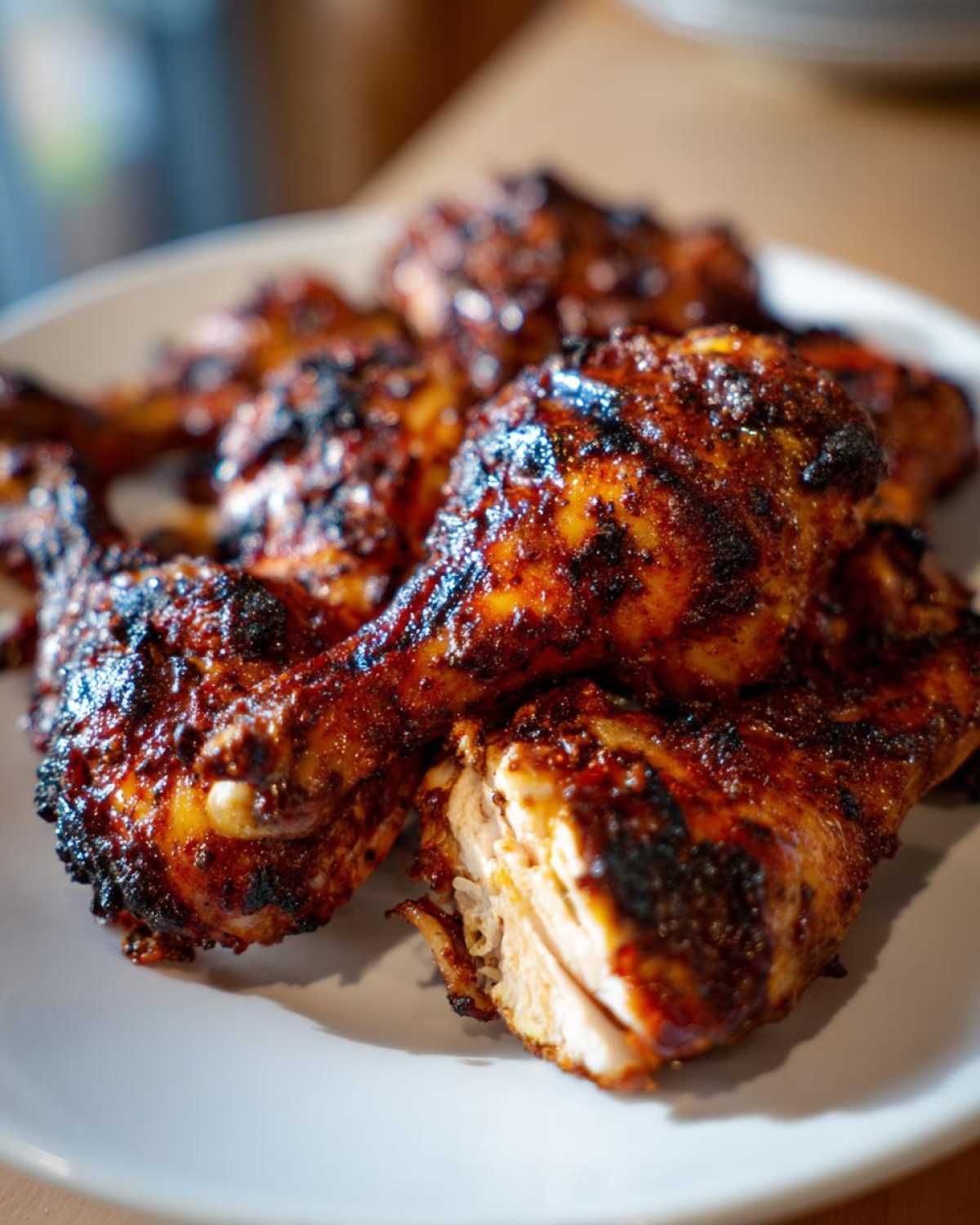 Close-up of grilled Jamaican jerk chicken pieces piled on a white plate, showing charred, spicy exterior and juicy interior.