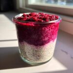 Close-up of layered raspberry chia pudding showing the white chia base and bright pink raspberry topping in a glass jar.