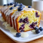 A close-up of sliced lemon blueberry bread topped with a white glaze and fresh blueberries.