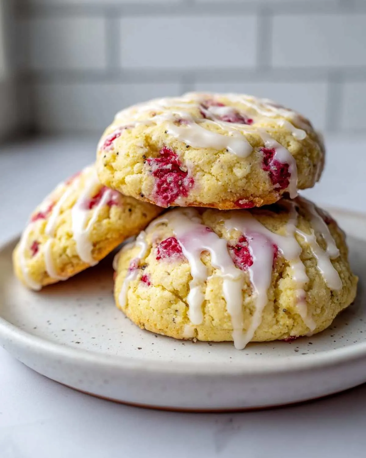 A stack of three delicious lemon raspberry cookies topped with a thick white glaze, featuring visible raspberry pieces and poppy seeds.