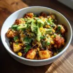 A close-up of loaded southwest potato bowls featuring seasoned potatoes, black beans, corn, melted cheese, fresh cilantro, and sliced avocado.