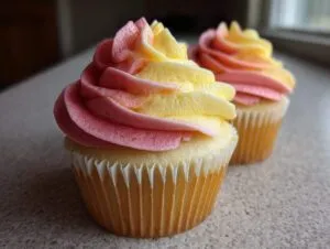 Close-up of two mango strawberry sunset cupcakes featuring pink and yellow swirled frosting.