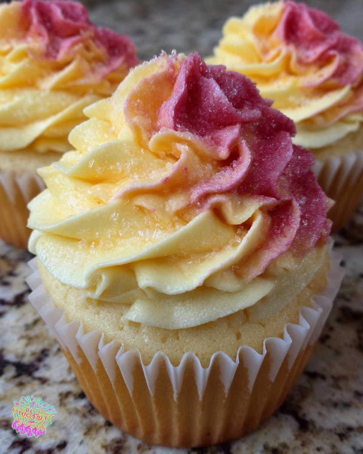 Close-up of a mango strawberry sunset cupcakes featuring yellow and pink swirled frosting topped with sugar crystals.