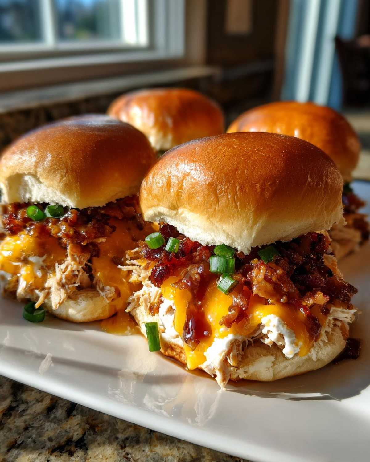 Four delicious maple chicken bacon sliders piled high with shredded chicken, melted cheese, bacon bits, and green onions.