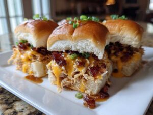 Close-up of several maple chicken bacon sliders featuring shredded chicken, melted cheddar cheese, and bacon bits on soft rolls.