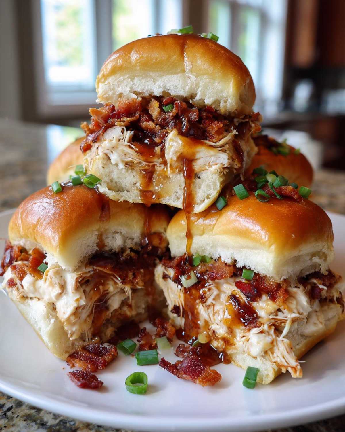 A stack of delicious maple chicken bacon sliders overflowing with shredded chicken, bacon bits, and maple glaze, garnished with green onions.