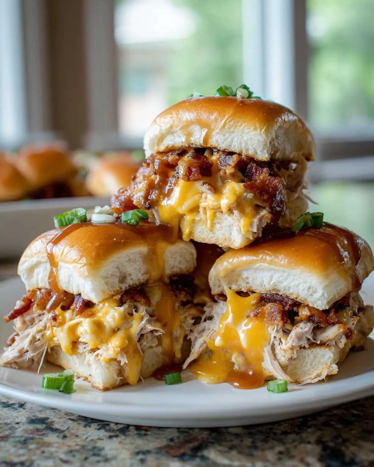 A stack of three messy maple chicken bacon sliders overflowing with melted cheddar cheese and crispy bacon.
