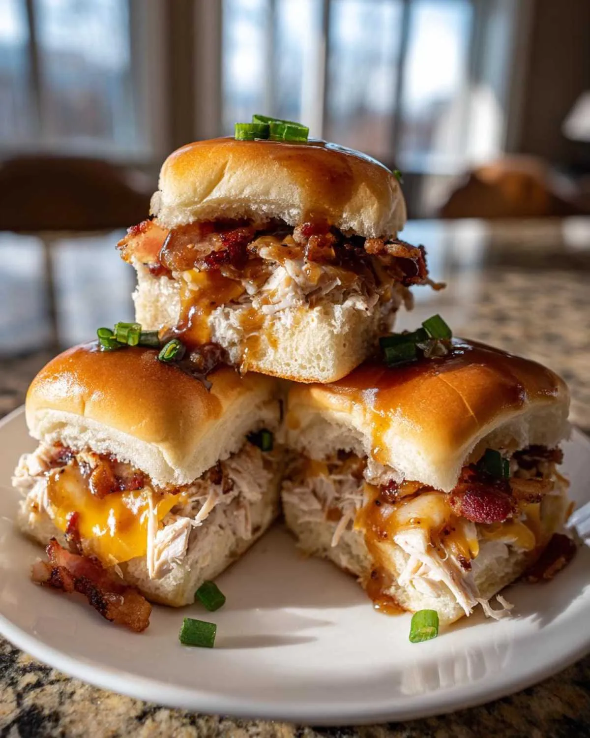 A stack of three maple chicken bacon sliders, featuring shredded chicken, melted cheese, bacon, and a sweet glaze, garnished with green onions.
