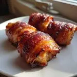 Four pieces of glazed maple garlic bacon chicken wrapped tightly and cooked until caramelized, resting on a white plate.