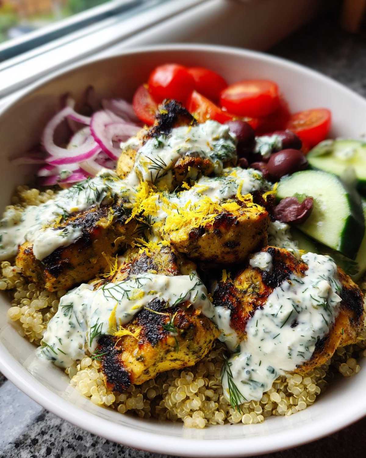 Close-up of mediterranean lemon-dill chicken bowls featuring grilled chicken, quinoa, tzatziki sauce, and fresh vegetables.
