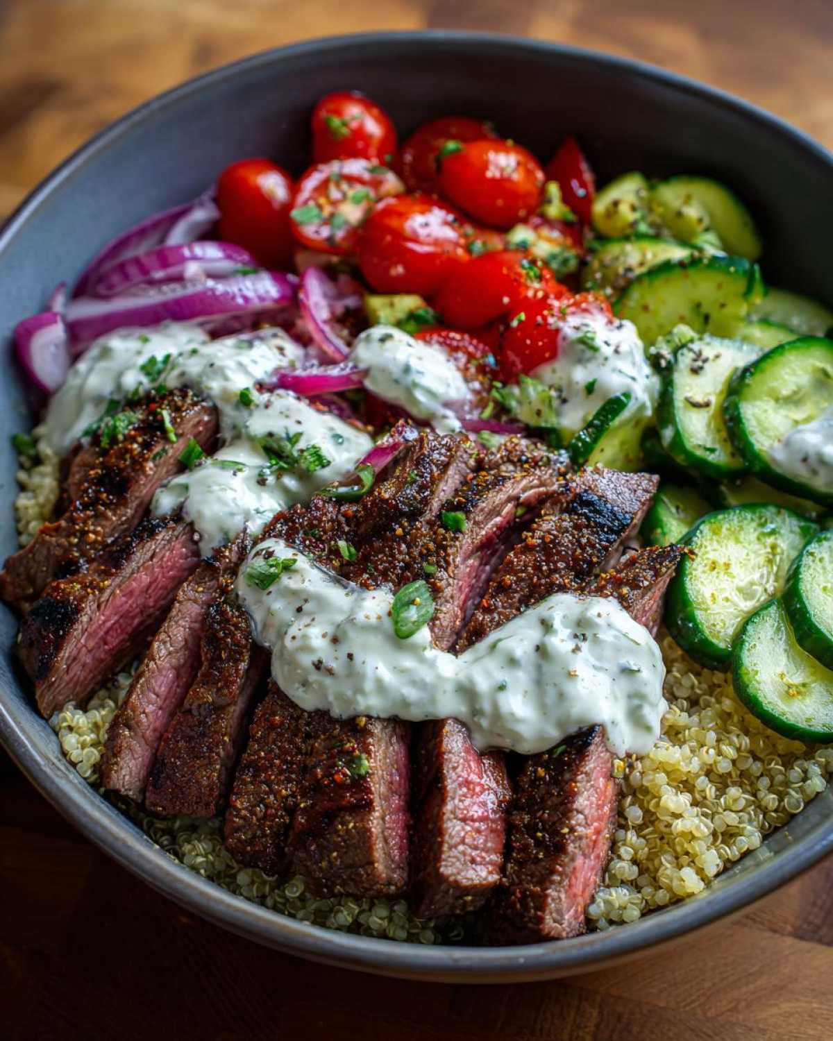 Close-up of perfectly sliced, seasoned steak served over quinoa in a mediterranean steak bowl with tzatziki sauce.