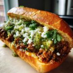 A delicious Mexican chopped cheese sandwich overflowing with seasoned meat, green salsa, and crumbled white cheese on a toasted roll.