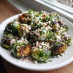 Close-up of roasted Mexican street corn Brussels sprouts topped with creamy sauce, crumbled cheese, and chili powder.