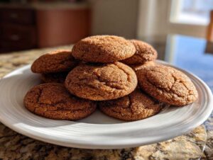A stack of freshly baked, soft applesauce cookies rolled in sugar, sitting on a white plate.
