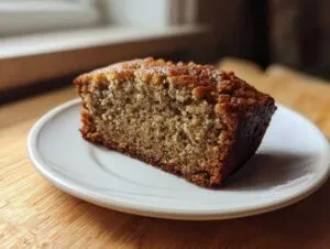 A close-up of a moist slice of banana bread recipe on a white plate, showing its rich brown crust.
