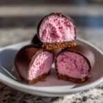 Close-up of no-bake pink velvet cheesecake bites cut in half, showing the pink filling and chocolate coating.