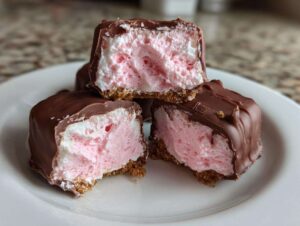 Close-up of three no-bake pink velvet cheesecake bites stacked, showing the pink filling, graham cracker crust, and chocolate coating.