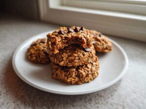 A stack of three chewy oatmeal chocolate chip breakfast cookie, with the top one broken open, sitting on a white plate.