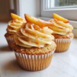 Three decadent peach bellini cupcakes topped with swirl frosting, peach drizzle, and a fresh peach slice.