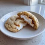 Two halves of a sugar cookie showing the gooey, melted filling of a peep stuffed easter cookie on a white plate.
