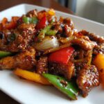 Close-up of glazed, saucy pepper chicken stir fry pieces mixed with colorful bell peppers and onions.