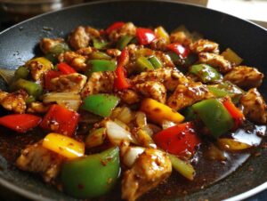 Close-up of colorful pepper chicken stir fry with chunks of chicken, red, green, and yellow peppers, and onions coated in a dark sauce.
