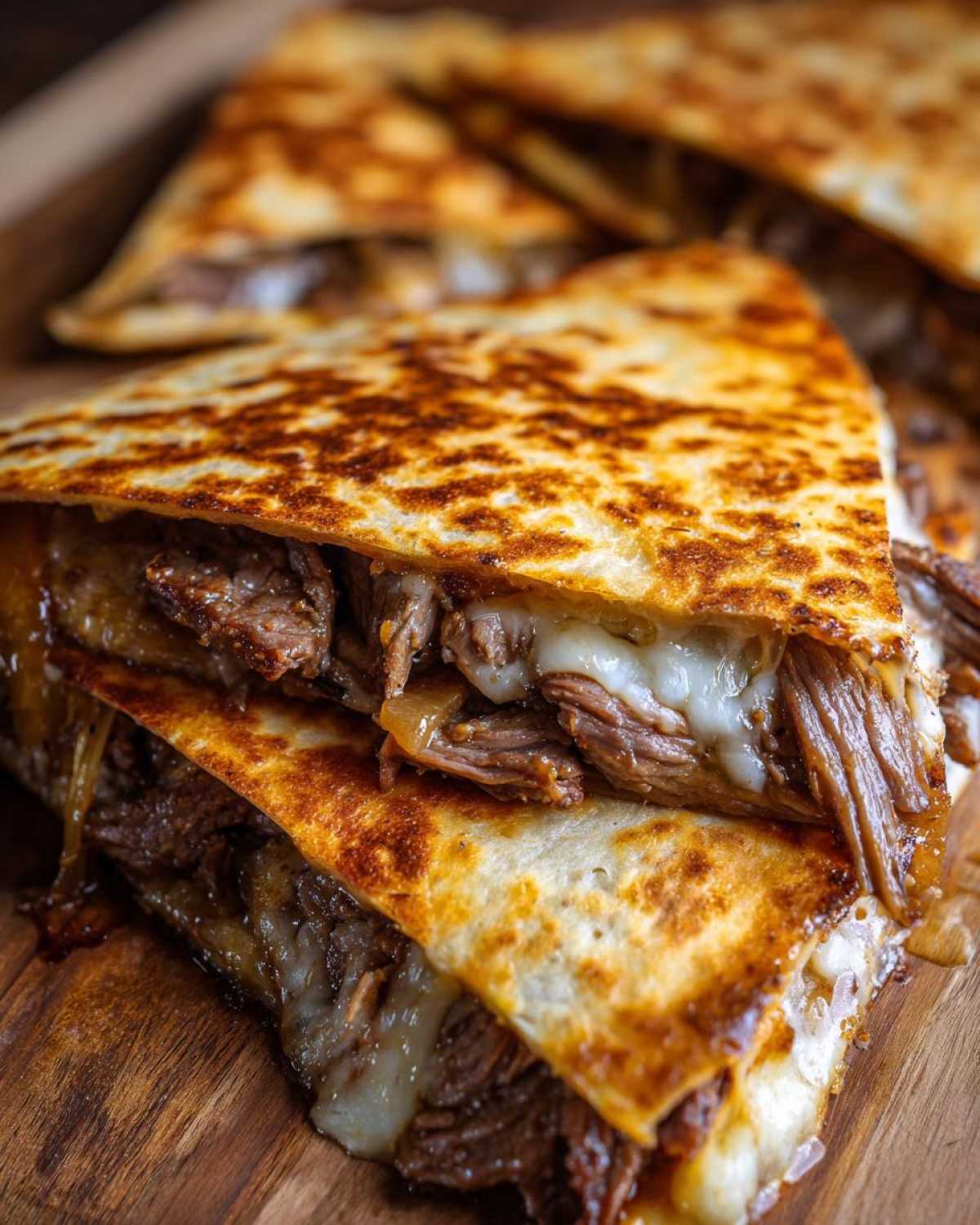 Close-up of crispy, golden-brown Philly cheesesteak quesadillas cut into wedges, showing melted cheese and shredded steak filling.