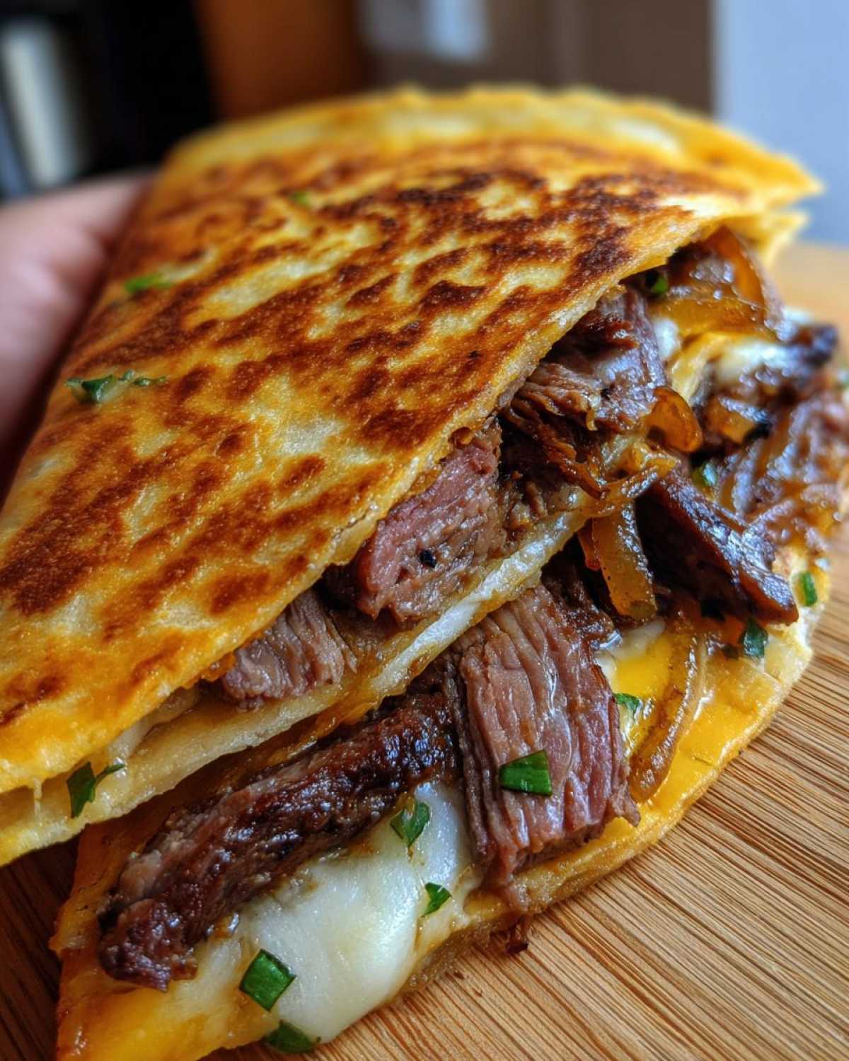 Close-up of a folded, grilled tortilla filled with steak, melted cheese, and caramelized onions for philly cheesesteak quesadillas.