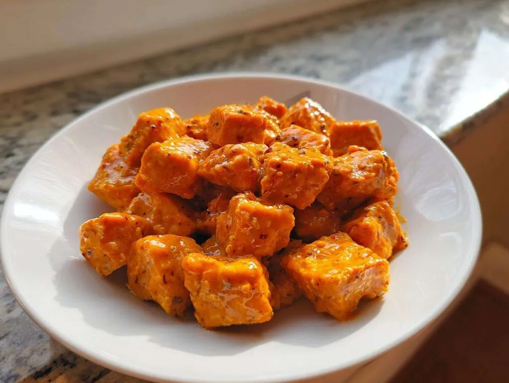 A white bowl filled with bite-sized pieces of salmon coated in a creamy, orange Bang Bang salmon sauce.