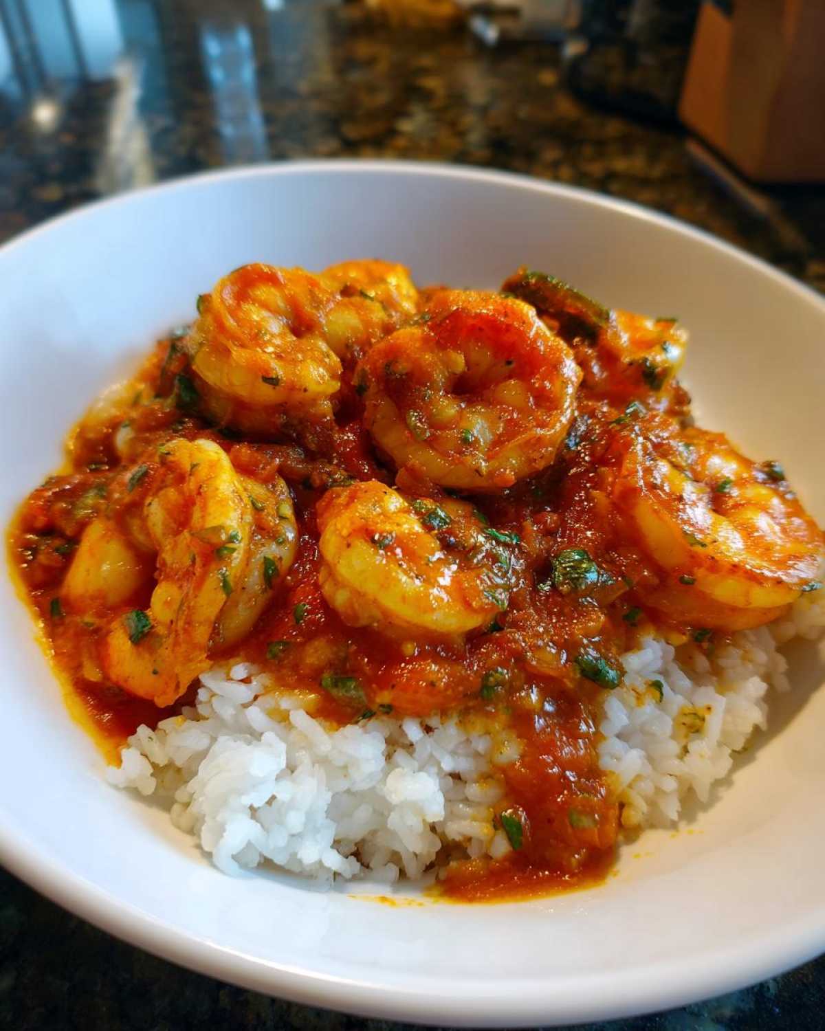 A close-up photo of a white bowl filled with white rice topped generously with saucy shrimp creole.