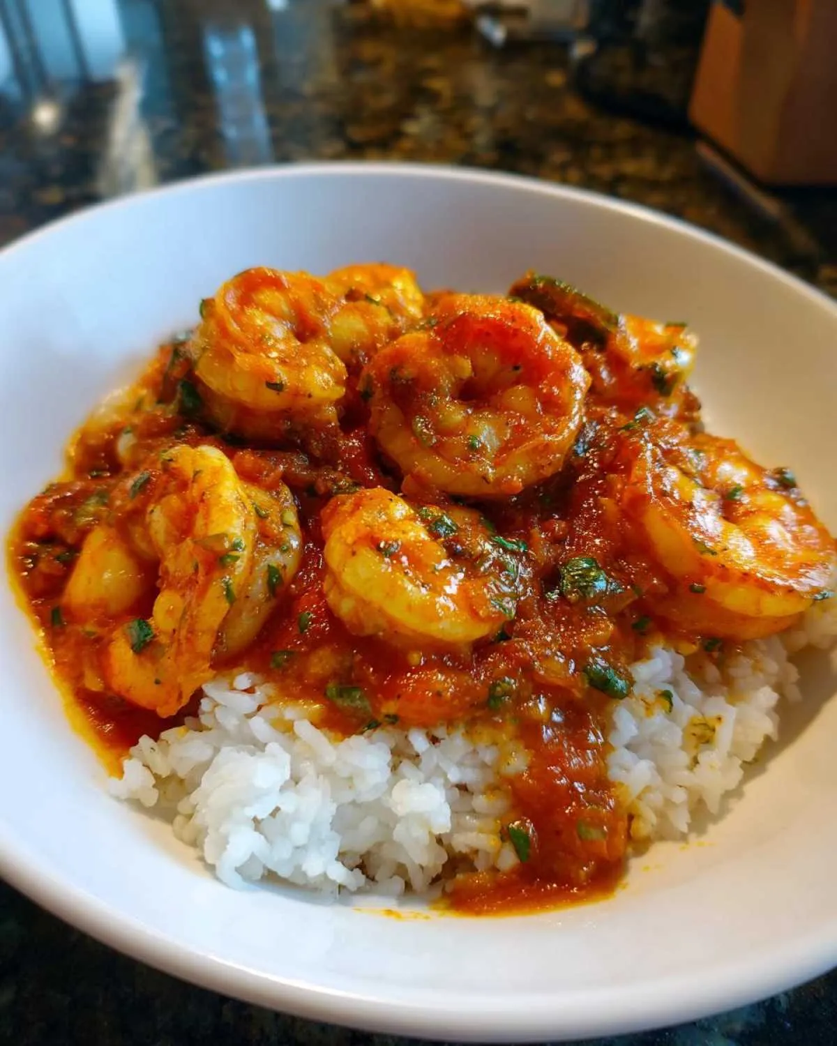 A close-up photo of a white bowl filled with white rice topped generously with saucy shrimp creole.
