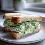 Two halves of quick cucumber salad sandwiches filled with creamy spread, sliced cucumbers, and fresh dill on white bread.