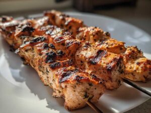 Close-up of perfectly grilled ranch garlic parmesan chicken skewers resting on a white plate, showing char marks and herbs.