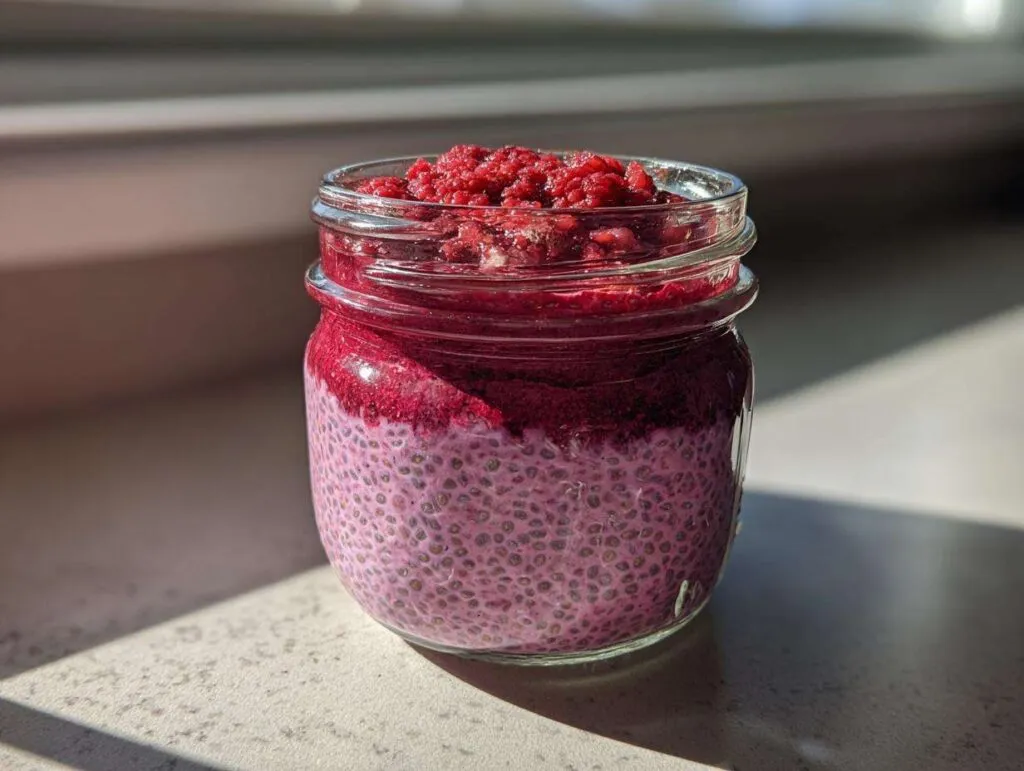 Close-up of layered raspberry chia pudding texture in a glass jar, topped with crushed raspberries.