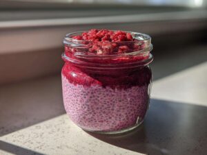 Close-up of layered raspberry chia pudding texture in a glass jar, topped with crushed raspberries.