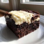 A close-up of a rich, dark chocolate root beer float brownies square topped with white frosting.