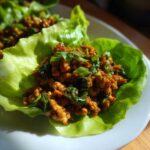 Close-up of savory chicken lettuce wraps filling served in a crisp butter lettuce cup, garnished with green onions.